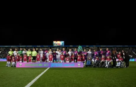Les joueurs de deux équipes de football posent avec des enfants, dont certains en fauteuil roulant, derrière une banderole de sensibilisation aux maladies rares.