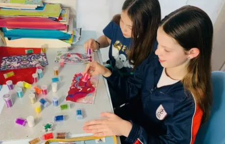 Deux élèves du COAMI appliquent des paillettes de couleur sur leurs dessins en classe.