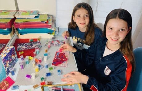 Carolina et une camarade décorent des dessins de licornes avec des paillettes, à l’école.