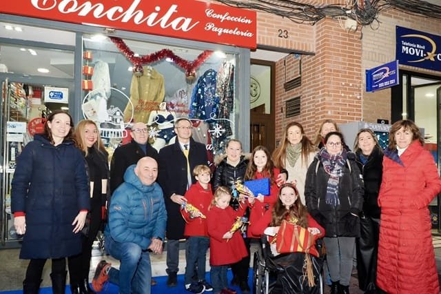 Photo de groupe devant la boutique Conchita, avec des enfants en manteau rouge et une fille en fauteuil roulant devant.