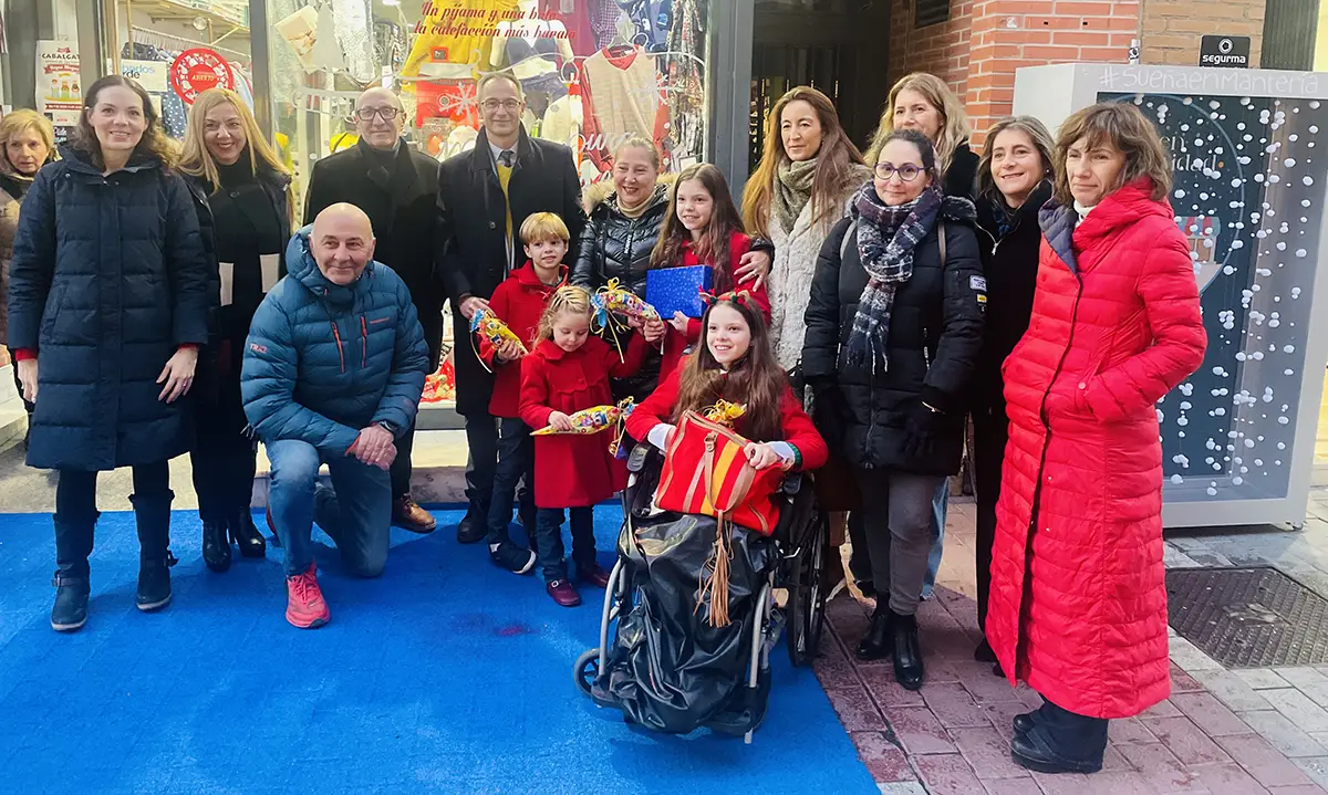 Photo de groupe devant une boutique de la rue Mantería décorée pour Noël, une fille en fauteuil roulant au centre.