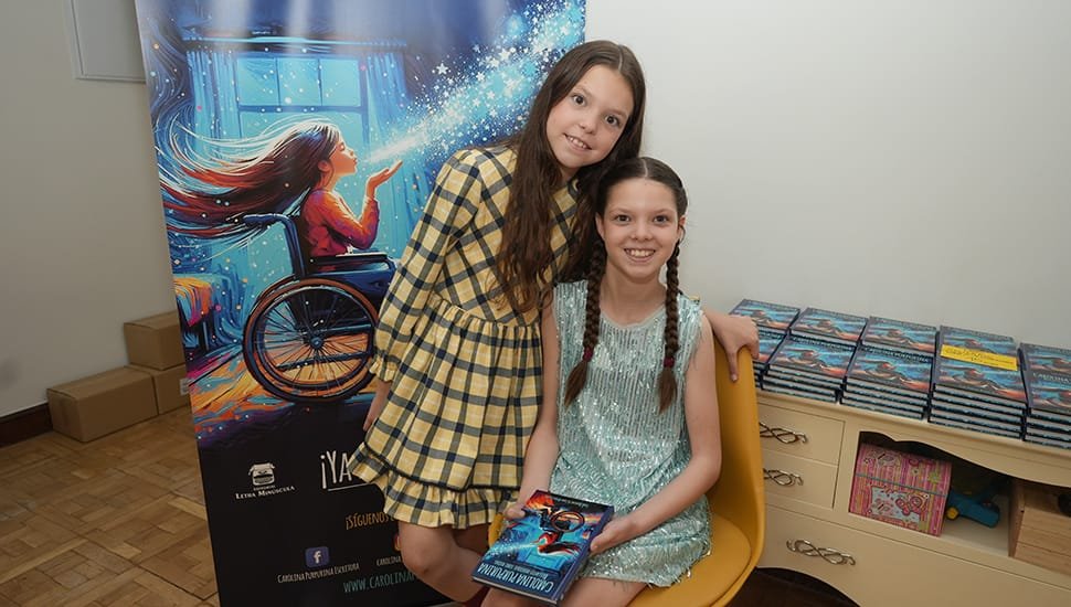 Deux filles posent près du kakémono du livre ; l’une tient un exemplaire, des piles de livres derrière elles.