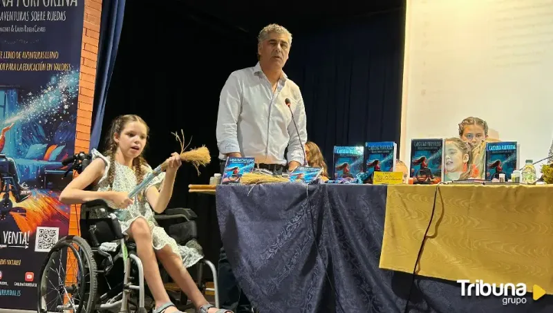 Présentation dans une salle : une fille en fauteuil roulant tient un balai de paille près de la table des exemplaires.