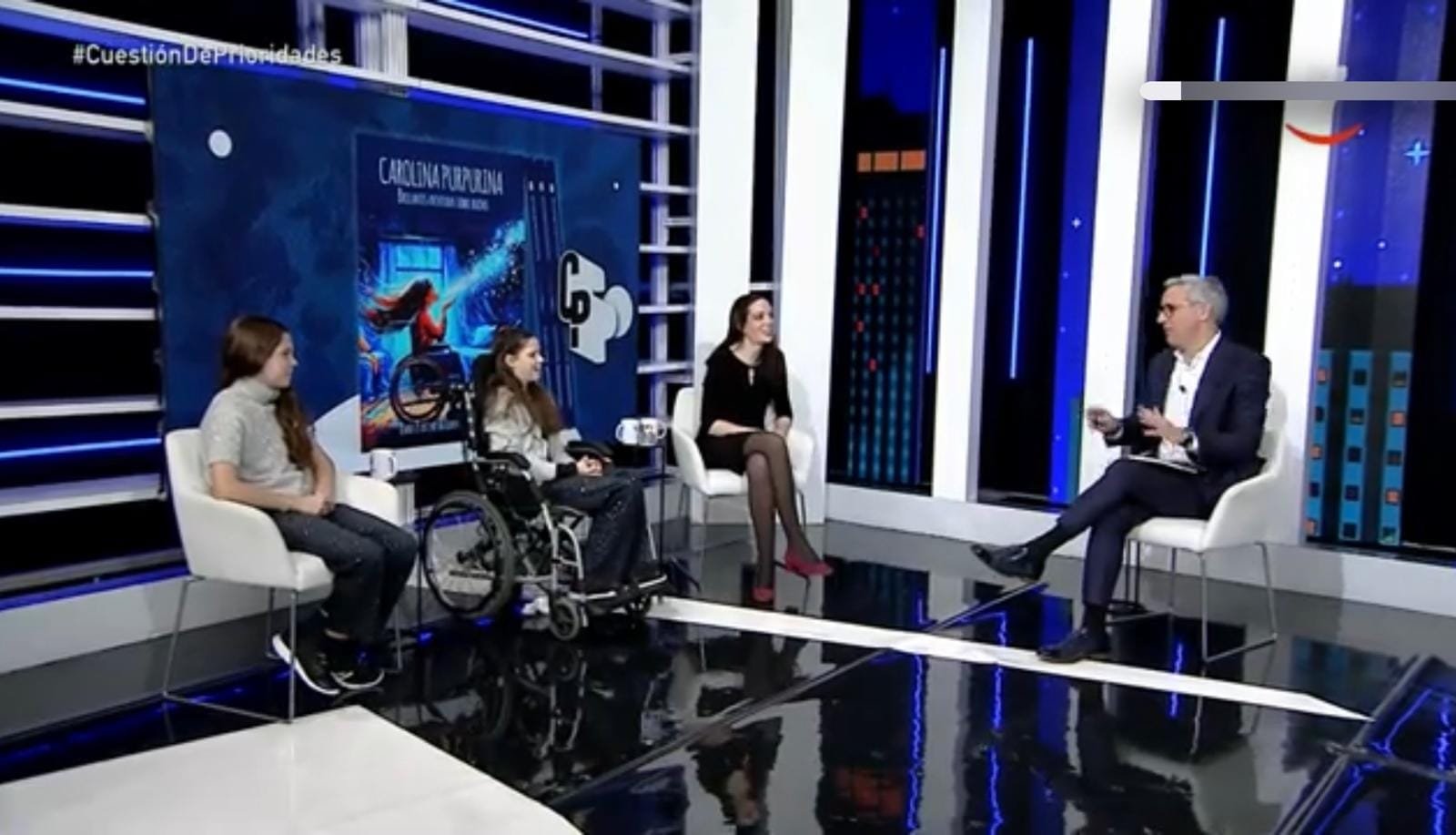 Plateau de télévision : deux filles, dont une en fauteuil roulant, et une femme face au présentateur, devant la couverture du livre.