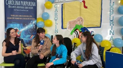 Interview de COPE dans une école : une journaliste au micro avec Carolina et deux autres filles, devant le kakémono du livre.