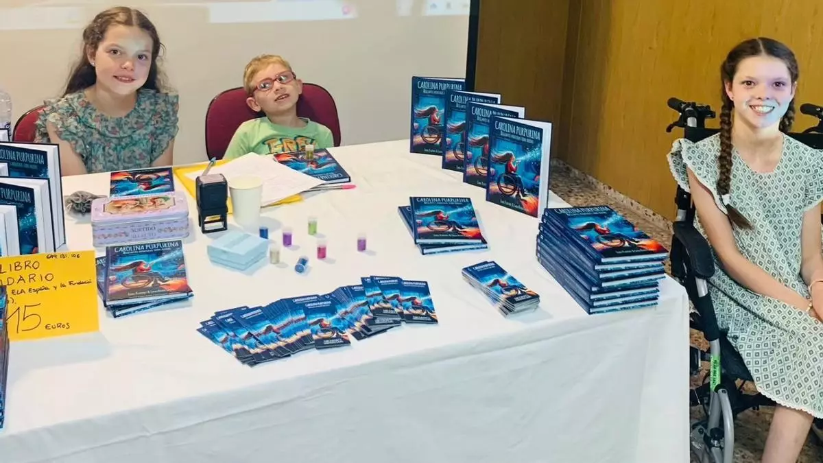Table de dédicace avec des piles du livre, des marque-pages et des tubes de paillettes ; à droite, une fillette en fauteuil roulant.