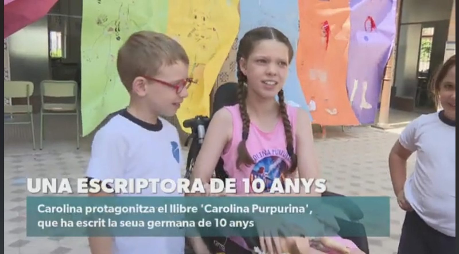 Image du journal d’À Punt : Carolina, en t-shirt du livre, échange avec un garçon dans la cour de l’école.