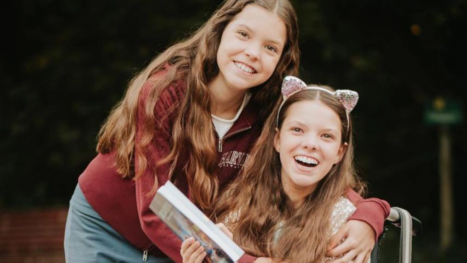 Isabel enlace Carolina, qui rit avec le livre entre les mains, dans un parc.