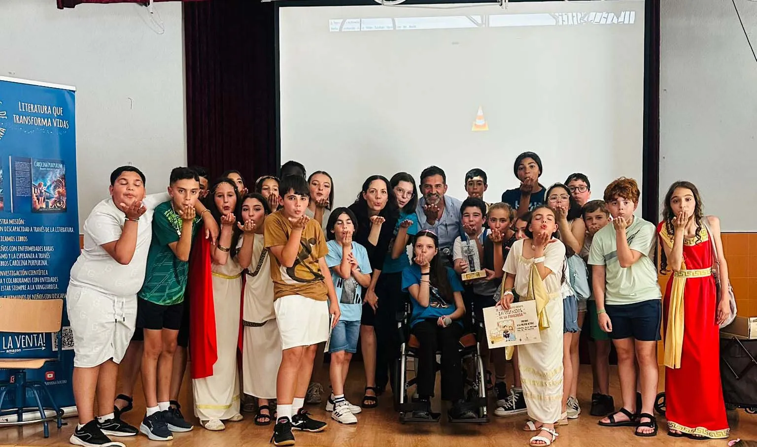 Élèves et enseignants soufflent des paillettes autour de Carolina, qui tient le diplôme à côté du trophée.