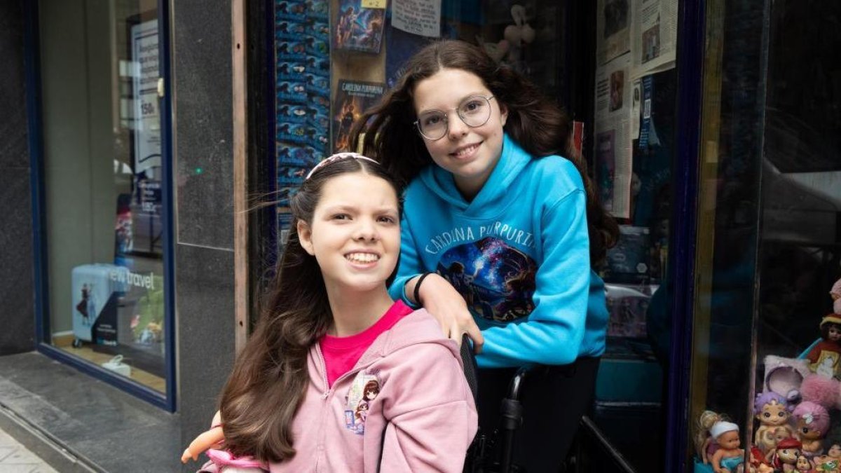 Carolina, dans son fauteuil roulant, et Isabel, en sweat Carolina Purpurina, posent devant une vitrine où sont exposés les livres de la saga.