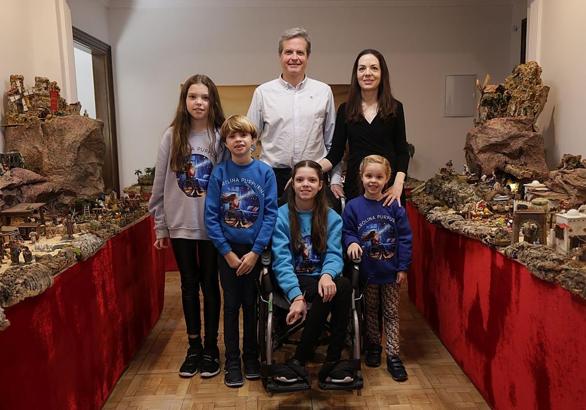 Deux adultes et quatre enfants en sweat-shirts Carolina Purpurina posent entre les tables de la crèche ; au centre, Carolina, dans son fauteuil.