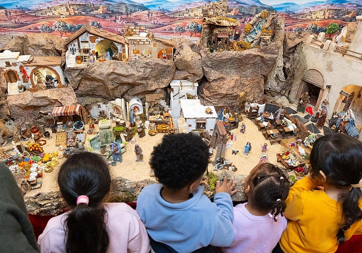 Premiers visiteurs de la crèche : quatre enfants, de dos, se penchent sur son paysage de rochers, de maisons et de figurines.